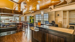 Un grand espace bar avec un plafond en bois, un comptoir doté d’une caisse enregistreuse et un coin salon avec des chaises.