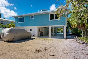 Une maison à deux étages avec un patio couvert, un abri pour bateau et un ciel d’un bleu limpide.