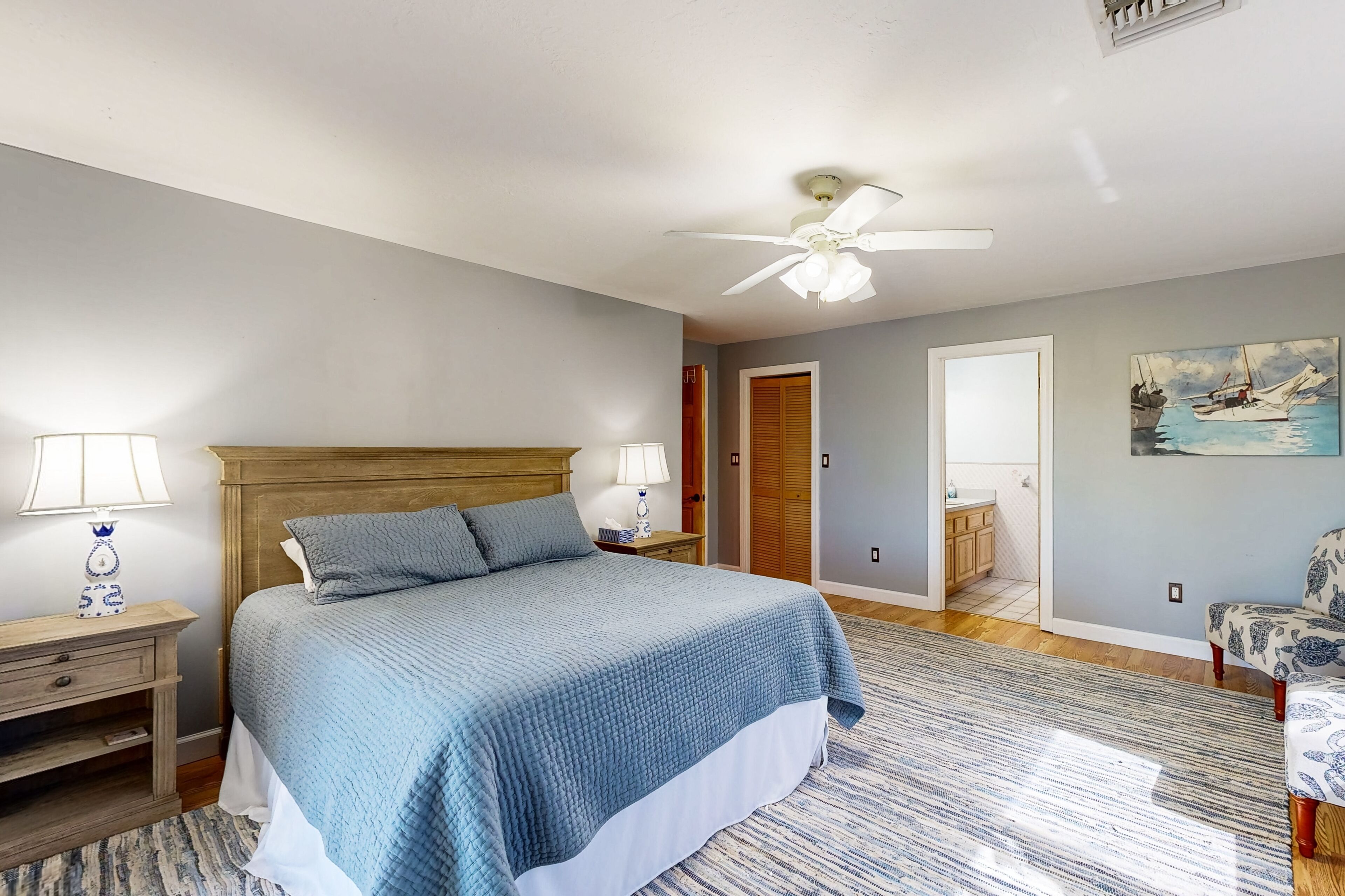 A bedroom with a bed, nightstands, a ceiling fan, a door, and a painting on the wall.