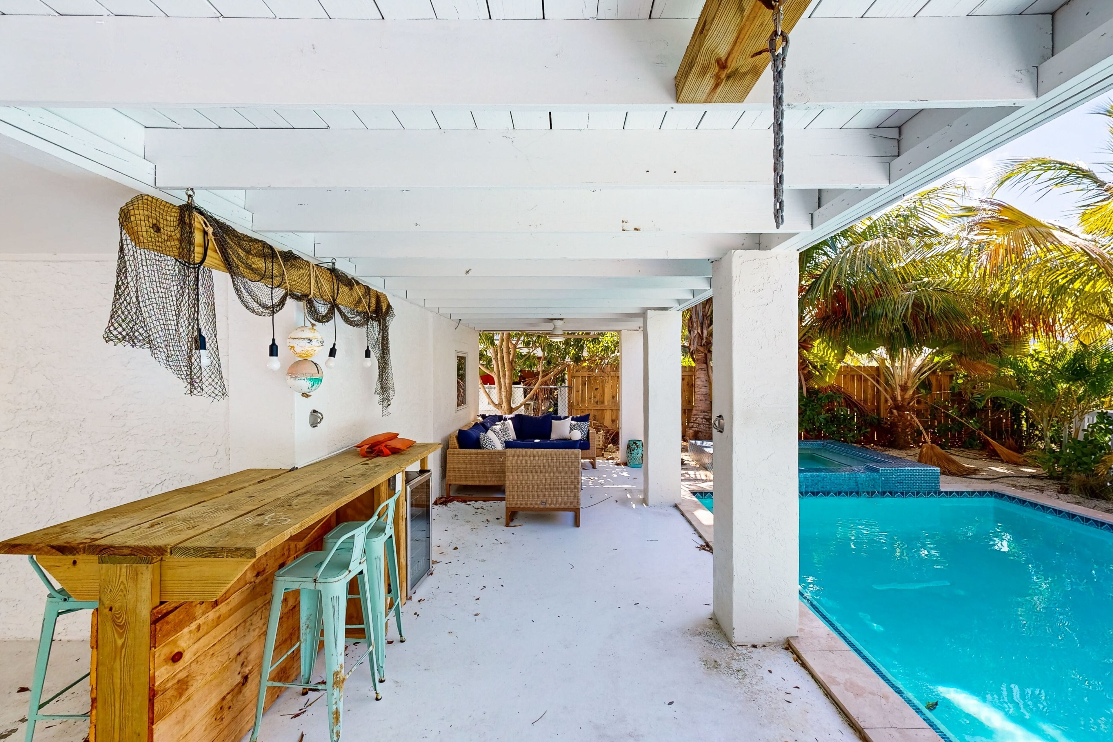 A covered outdoor area with a pool, wooden table, chairs, and a sofa.
