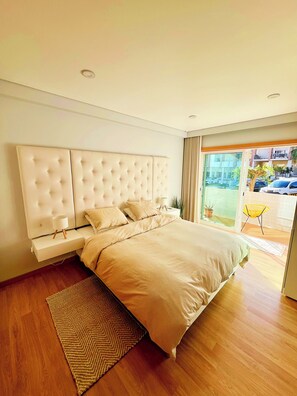 A modern bedroom with a large bed, a bedside table, and a view of the outside. - Casa Betz Alvor - 2 Bedrooms Apartment | Pool | Near Beach | Indoor Garage (Alvor)