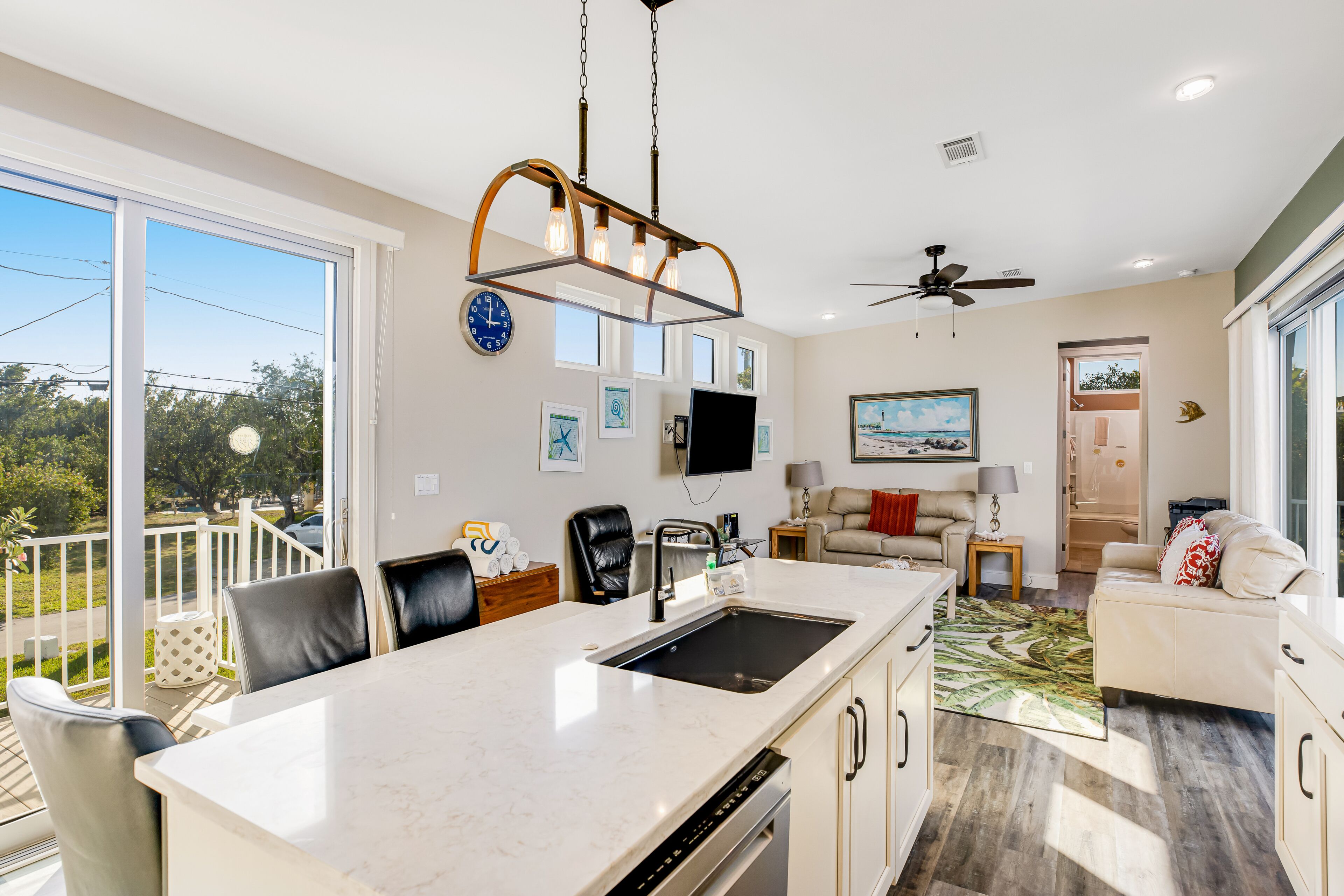 A modern kitchen with a large island, a dining area with a white table and chairs, and a living room with a sofa and a TV.