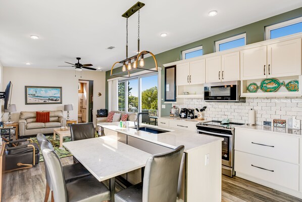 A modern kitchen with white cabinets, a central island, and a dining area with a table and chairs. - Beautiful waterfront home with central AC, dock, lovely balcony & patio (Big Pine Key)