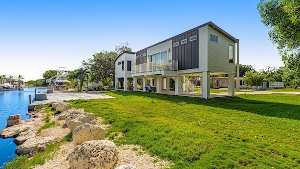 Une maison moderne à deux étages, dotée d’un grand balcon, d’une piscine et d’une pelouse bien entretenue.