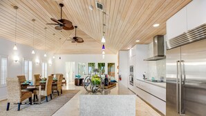 Una cocina amplia con un refrigerador moderno de acero inoxidable, techo de madera y un comedor con sillas de mimbre y una mesa de mármol.