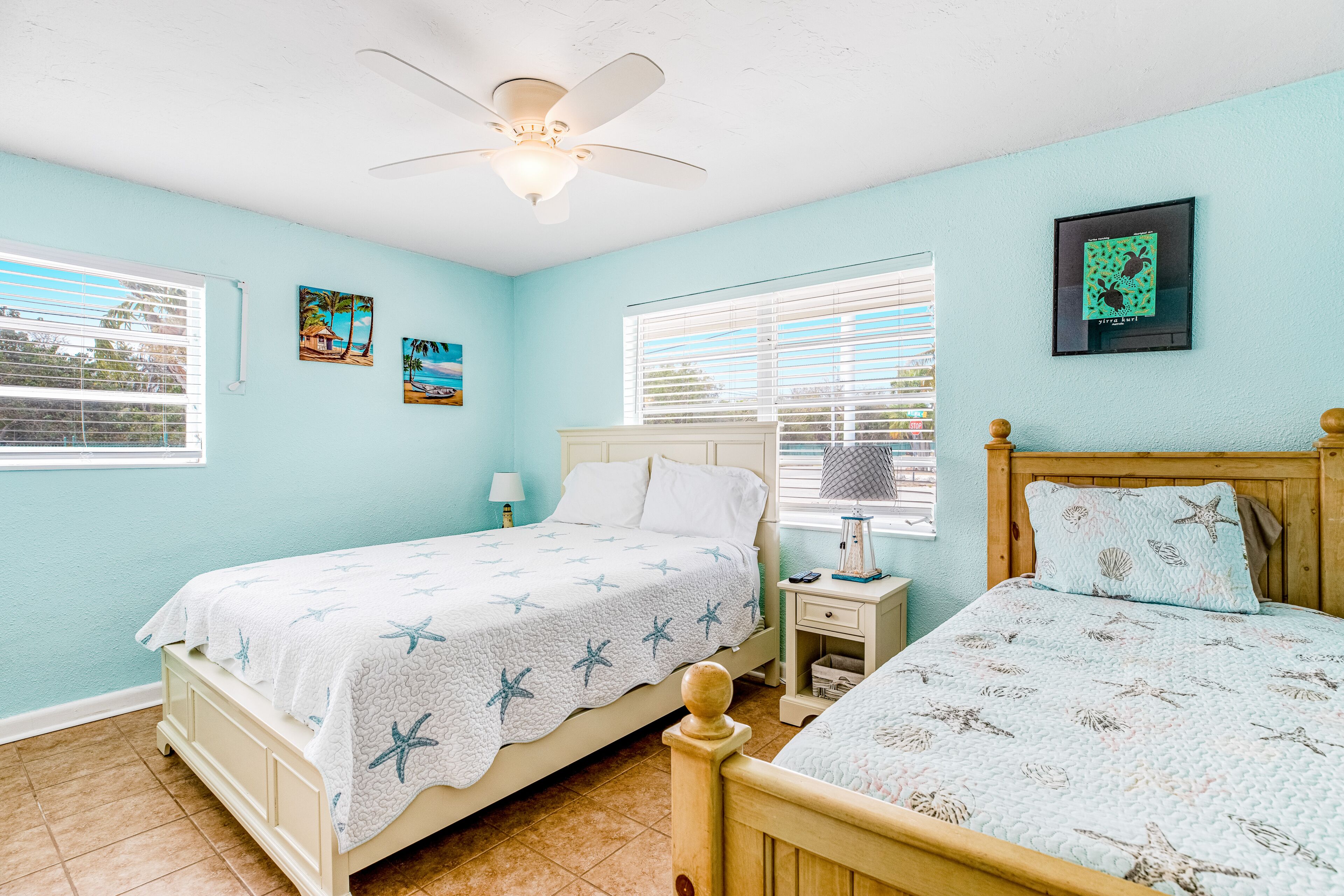 A bedroom with two beds, a ceiling fan, and artwork on the walls.