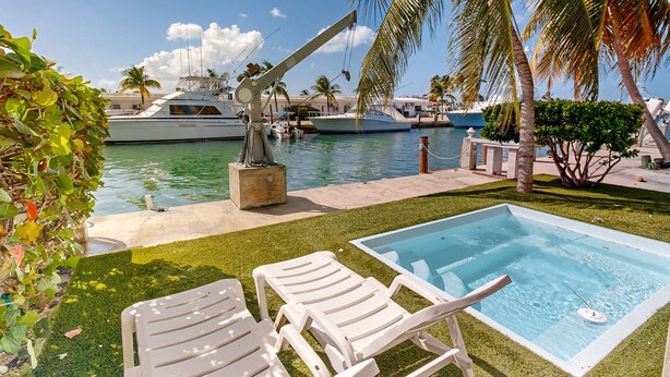 A pool area with lounge chairs, a small pool, and a marina with boats in the background. - Waterfront Half-Duplex with 30-Ft. Dock, Sitting Pool, and Private Beach Access (Key Colony Beach)