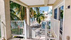 A covered outdoor area with a white railing, palm trees, and a view of a building with a blue roof. - Waterfront Half-Duplex with 30-Ft. Dock, Sitting Pool, and Private Beach Access (Key Colony Beach)