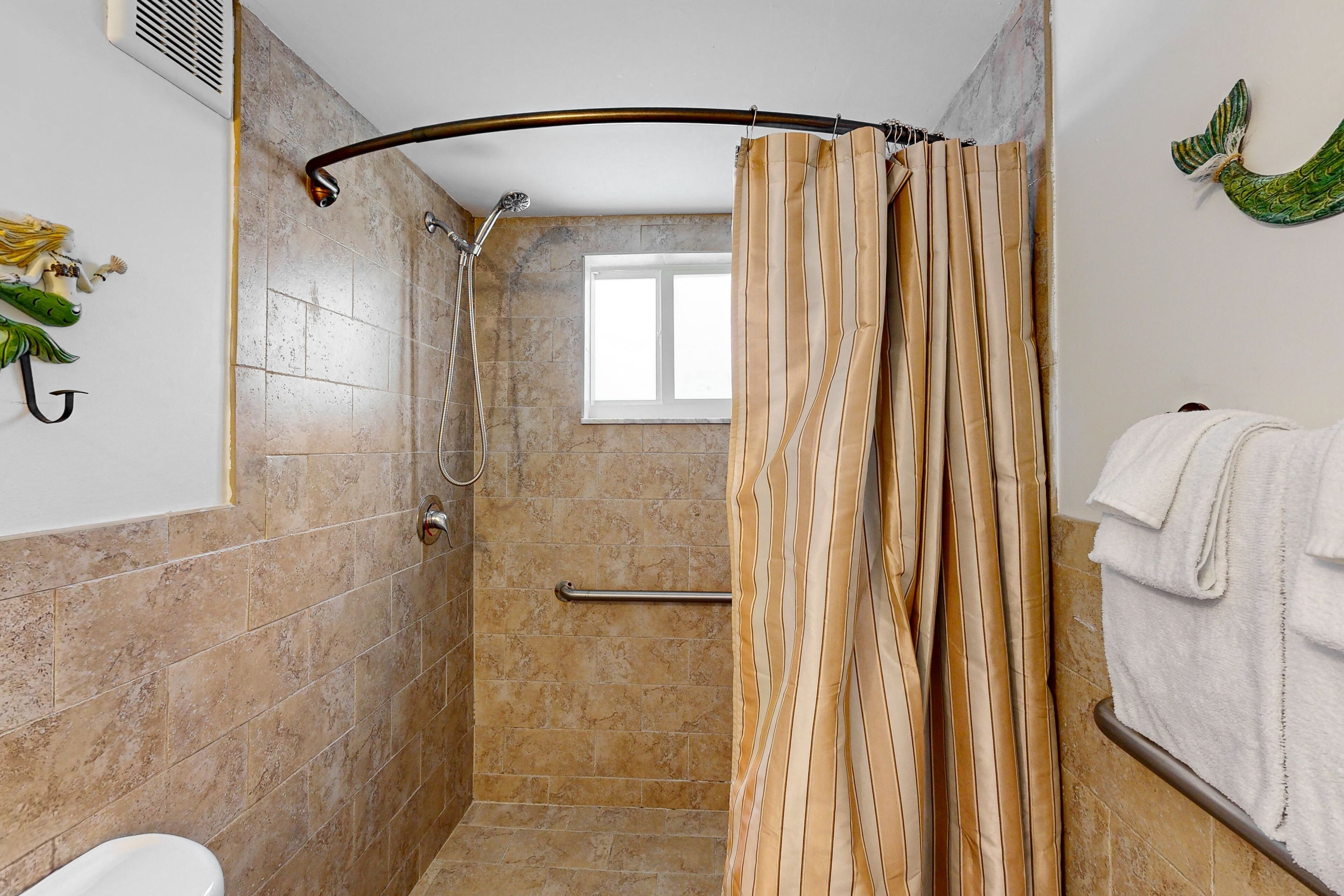 A shower with a curved showerhead, a window, and a towel rack.