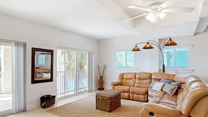 A spacious living room with a leather sofa, a small wicker coffee table, and a ceiling fan. - Waterfront Half-Duplex with 30-Ft. Dock, Sitting Pool, and Private Beach Access (Key Colony Beach)