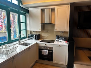A compact kitchen with a sink, stove, and toaster, a window with a stained glass view, and a television mounted on the wall. - Temple Bar Premium Apartments (Dublin)