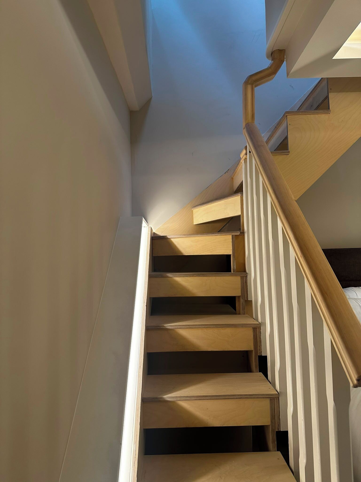 Una escalera de madera con barandillas blancas y un tragaluz arriba.