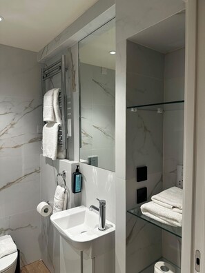 A modern bathroom with a marble wall, a glass shower enclosure, a white sink, and a toilet. - Temple Bar Premium Apartments (Dublin)