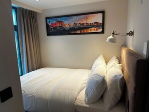 A hotel room with a bed, a painting of a bridge, a lamp, and a window with curtains. - Temple Bar Premium Apartments (Dublin)