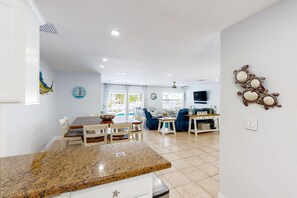 A modern kitchen with granite countertops, a dining area with a wooden table and chairs, a living room with a sofa and TV, and a decorative wall piece. - Waterfront home with private heated pool, dock, canal views, grill, AC (Marathon)