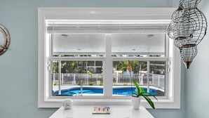 Et værelse med et hvidt skrivebord, en potteplante og udsigt til en swimmingpool gennem et stort vindue.