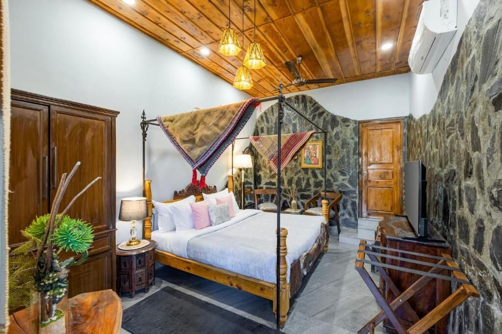 A four-poster bed with a canopy, a wooden wardrobe, a television, and a stone wall.