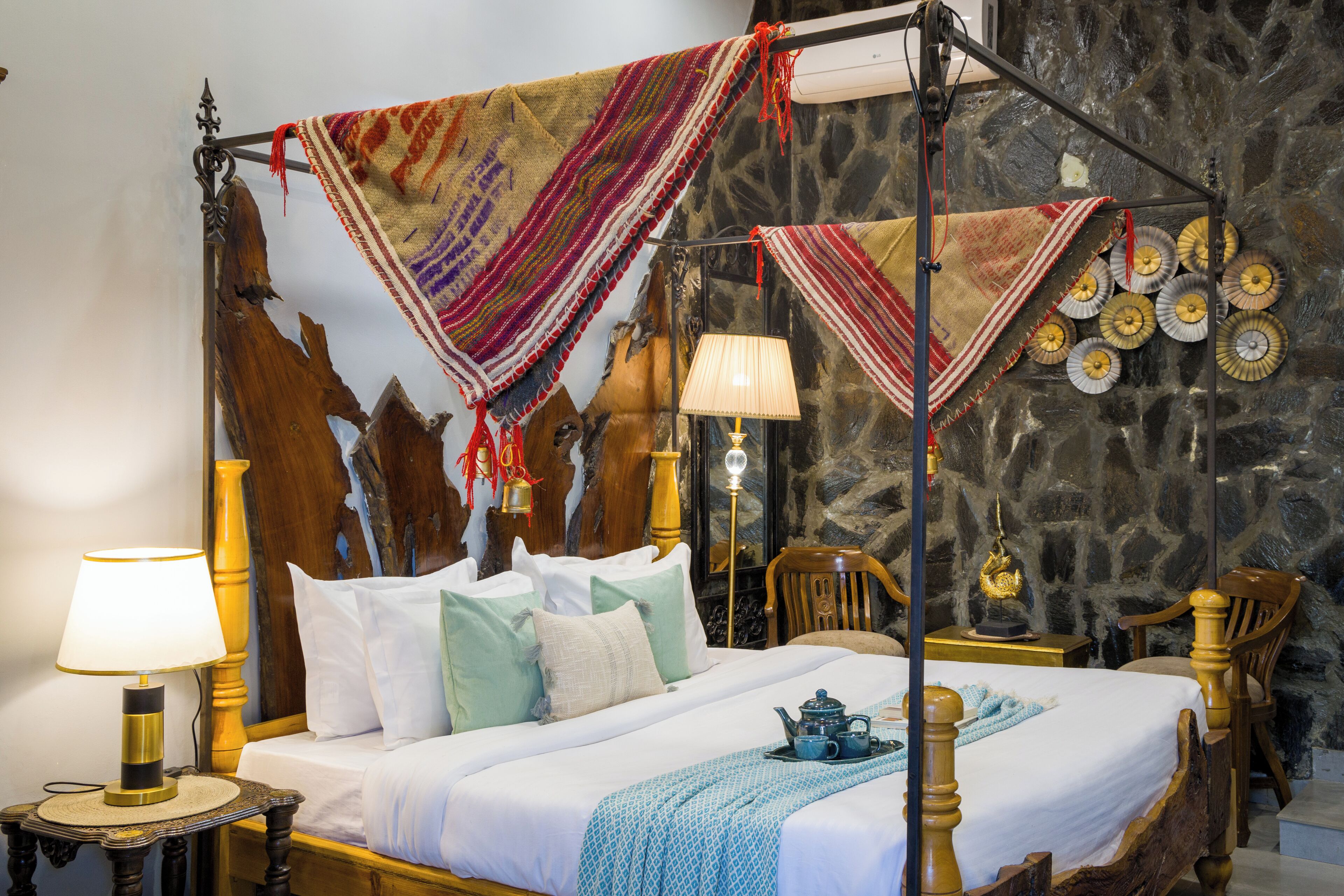 A four-poster bed with a canopy, a bedside table with a lamp, a chair, and a decorative wall with plates.