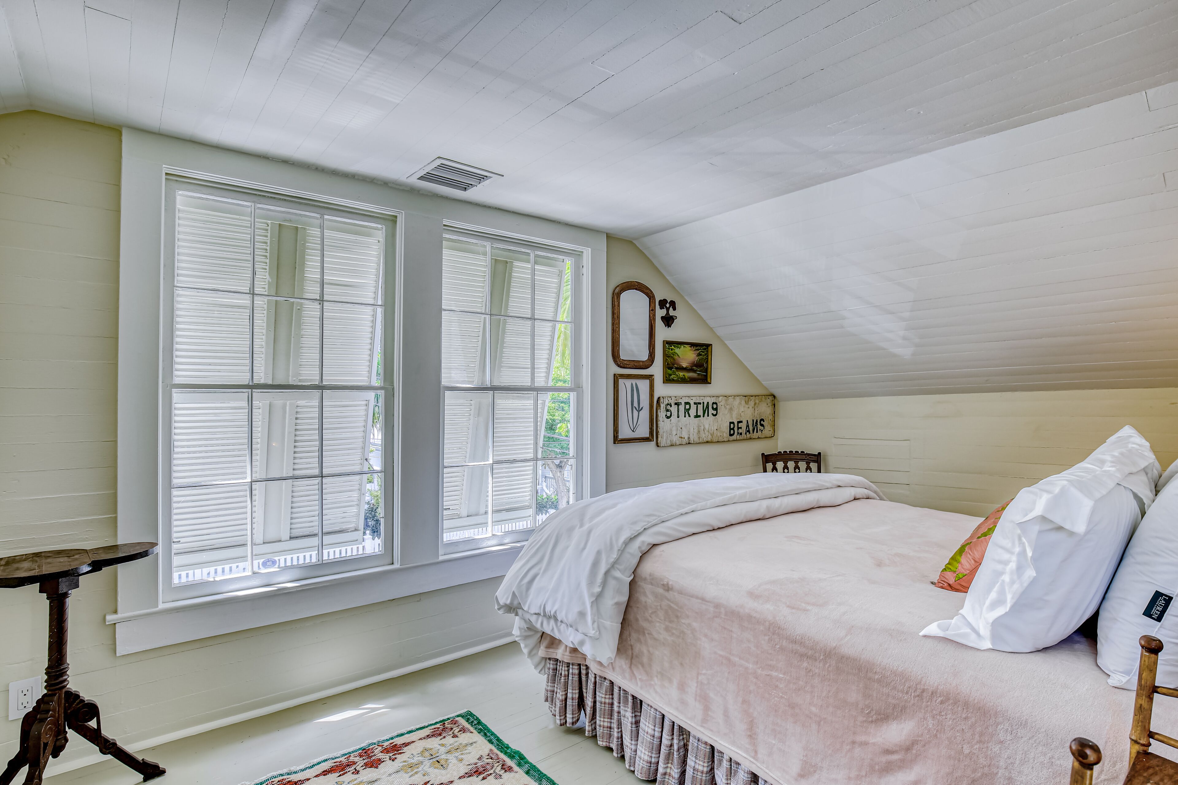 A bedroom with a large window, a bed with white bedding, a wooden headboard, and a small table.