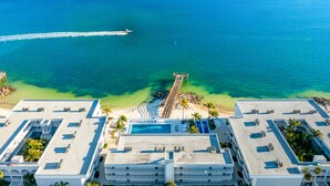 Eine Vogelperspektive zeigt ein Hotel mit einem Dachpool, einer ansteigenden Mole und einen Strandabschnitt mit Palmen.