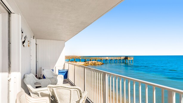 Ein Balkon mit weißen Korbmöbeln, Blick auf das Meer und ein Pier in der Ferne.