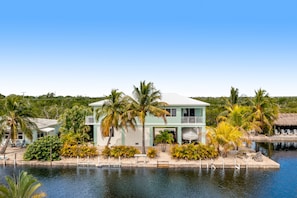 A two-story house with a pool, surrounded by palm trees and greenery.