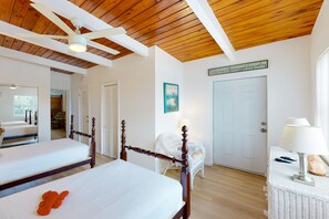 A bedroom with two beds, a ceiling fan, a white wicker chair, a bedside table with a lamp, and a door with a sign. - Saylor's Bay | House in Key Colony Beach with ocean views (Key Colony Beach)