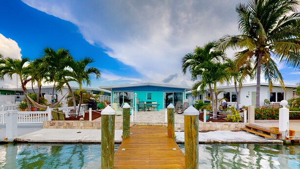 A wooden dock leading to a building with a blue facade, surrounded by palm trees and a clear sky. - Saylor's Bay | House in Key Colony Beach with ocean views (Key Colony Beach)