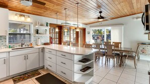 Une cuisine moderne avec des meubles blancs, un grand îlot central, des luminaires suspendus et un ventilateur de plafond.