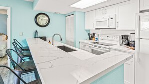 Una cucina con una grande isola, pensili bianchi, una sveglia e un forno a microonde.