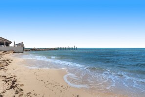 Ein Strand mit einer strohgedeckten Struktur, einem hölzernen Steg und blauem Himmel.