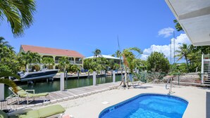 En swimmingpool med træterrasse, liggestole og en havn med både.