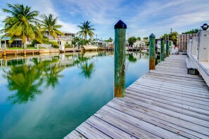 A wooden dock extending into calm water with reflections of palm trees and a clear sky. - Dog-Friendly Home with 60-Ft. Dock and Access to Cabana Club and Shared Pool (Key Colony Beach)