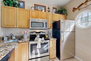 A kitchen with wooden cabinets, stainless steel appliances, a granite countertop, and a window.