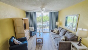 A living room with a ceiling fan, a sofa, a chair, a small table, and a window with curtains. - Resort condo with pool & hot tub, private parking (Key West)