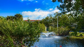A serene garden with a fountain, lush greenery, and a clear blue sky. - Resort condo with pool & hot tub, private parking (Key West)