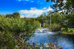 Un jardin paisible avec une fontaine, une végétation luxuriante et un ciel bleu azur.