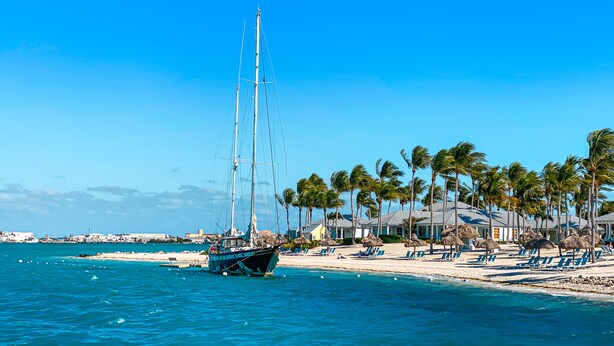 A beach with a sailboat, palm trees, and beach chairs. - Resort condo with pool & hot tub, private parking (Key West)