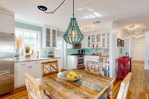 A modern kitchen with white cabinets, a wooden dining table with a bowl of lemons, and a decorative chandelier. - Bohemian island home full of color and modern amenities - in a great location (Key West)