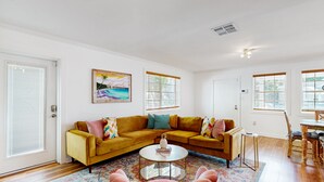 Ein Wohnzimmer mit einem gelben Sofa, einem rosa Sessel, einem Couchtisch und einem Bild an der Wand.