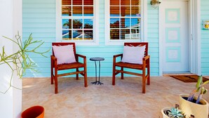 Eine Veranda mit zwei Holzstühlen, einem kleinen Tisch, einem Blumentopf und einer Tür mit einer Lampe.
