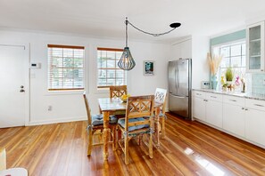 Uma cozinha moderna com piso de madeira, armários brancos, geladeira de aço inoxidável e uma mesa de jantar com cadeiras.