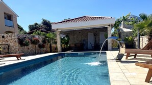 A swimming pool with a water feature, stone walls, and outdoor furniture. - Apartment Mariner 1 With Heated Pool (Nin)