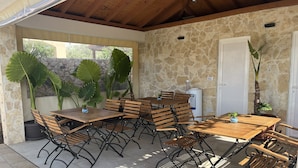 An outdoor patio with stone walls, wooden tables, and chairs. - Apartment Mariner 1 With Heated Pool (Nin)