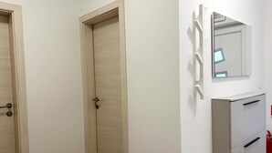 A room with two wooden doors, a white wall, a mirror, and a white cabinet with drawers. - Apartment Mariner 1 With Heated Pool (Nin)
