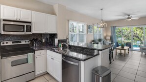A modern kitchen with white cabinets, a granite countertop, stainless steel appliances, and a view to a patio area. - Duck Key waterfront villa with private pool, kayak, SUP (Duck Key)