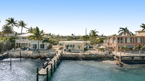 A coastal property with a dock, palm trees, and a stone wall. - Waterfront beauty with a dock, small private beach, washer/dryer, & gas grill (Key Colony Beach)