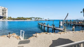 A waterfront dock with a pier extending into the water, surrounded by pebbles and a building in the background. - Waterfront beauty with a dock, small private beach, washer/dryer, & gas grill (Key Colony Beach)