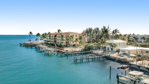 A coastal hotel with multiple buildings, a dock extending into the water, and palm trees. - Waterfront beauty with a dock, small private beach, washer/dryer, & gas grill (Key Colony Beach)