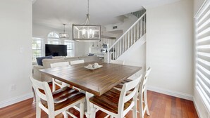 A dining area with a wooden table and white chairs, a chandelier, and a staircase leading to an upper level. - Waterfront home w/hot tub, gas grill, WiFi, AC, near attractions (Key Largo)